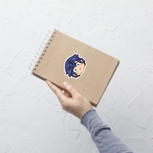 Fire Emblem sticker of Chrom (medium, 4x4) centered on a tan notebook against a white textured wall.