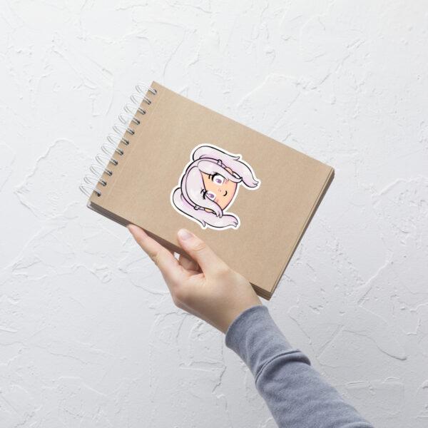 Fire Emblem sticker of Female Robin (medium, 4x4) shown on a kraft notebook against a white textured wall.