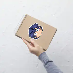 Fire Emblem sticker of Chrom (large, 5.5x5.5) displayed prominently on a brown spiral-bound notebook.