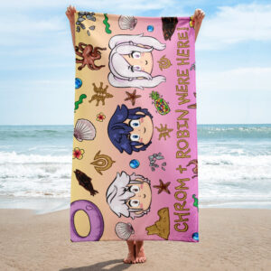 Person holding a Fire Emblem Towel with a vibrant Summer Scramble design on the beach, featuring chibi Chrom and Robin illustrations on a sunset-colored background.