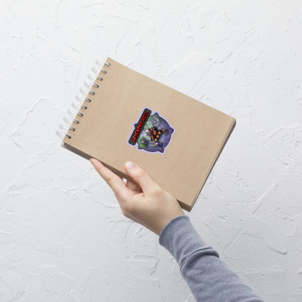 Close-up of a small Fire Emblem Sticker sheet featuring the Lavender Hell Sticker applied to a tan spiral notebook.