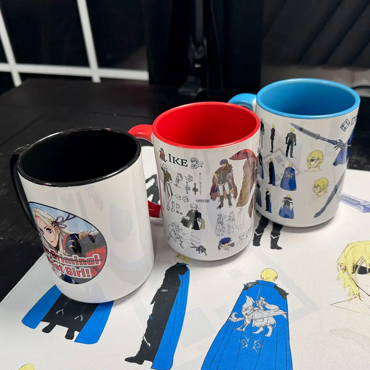 Three FEHology Fire Emblem mugs featuring Edelgard, Ike, and Dimitri designs, with black, red, and blue interiors.